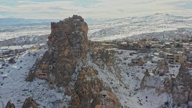 Aerial view of Uchisar Castle, a towering rock formation, contrasts with the soft white snow covering the landscape, Goreme, Cappadocia, Turkiye.