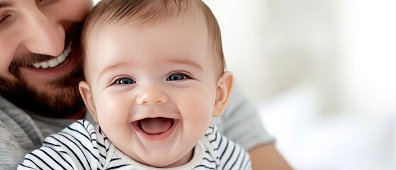 Happy baby smiles brightly while being held by father in a cozy bedroom setting with a soft background