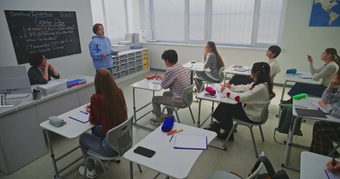 Teenage Boy in Blue Hoodie Confidently Presents Game Development Project Classmates and Teacher. Concept of Innovation in Education, and Building Public Speaking Skills Through Project Based Learning.