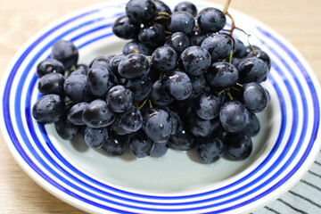 Close-up of fresh black grapes on a white plate with blue stripes. High-quality macro shot showcasing juicy berries, perfect for concepts of healthy eating, organic fruit, vegan diet, and natural food