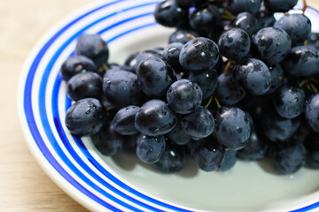 Close-up of fresh black grapes on a white plate with blue stripes. High-quality macro shot showcasing juicy berries, perfect for concepts of healthy eating, organic fruit, vegan diet, and natural food