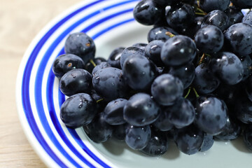 Close-up of fresh black grapes on a white plate with blue stripes. High-quality macro shot showcasing juicy berries, perfect for concepts of healthy eating, organic fruit, vegan diet, and natural food