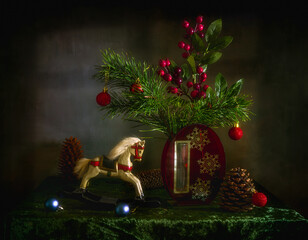 A branch with red berries, a prickly pine with cones, Christmas toys and a wooden horse. Festive mood. Waiting for a Christmas miracle.