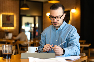 Fototapeta premium Man reviewing financial statements working in cafe