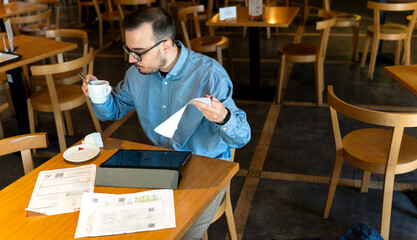 Man reviewing financial documents and drinking coffee in cafe