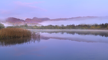 Misty Elterwater lake with peaceful reflections of mountains in The Lake District, UK.