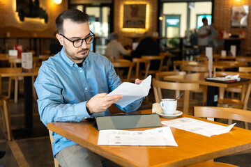 Man reviewing financial documents in cafe
