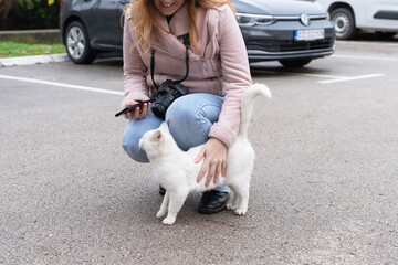A woman photographer is enjoying the company of a white cat in a parking lot