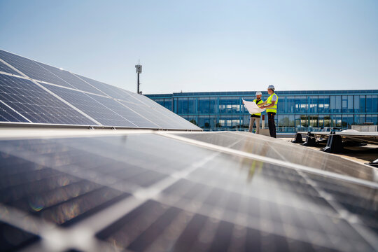 Two technicians discussing plan on the roof of a company building with solar panels
