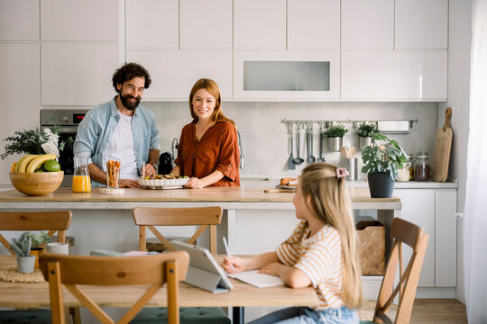 Family in kitchen with child using digital tablet for learning at home