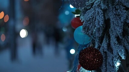 outdoors festive christmas tree branches covered in snow, decorated with colorful baubles and twinkling fairy lights, creating magical winter holiday atmosphere with bokeh lights on street. close up. - Powered by Adobe