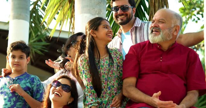 Indian family smiling on steps outdoors spending quality time together on green lawn, cheerful multi-generation portrait of grandparents, parents, and kids bonding, relaxing, enjoying leisure weekend
