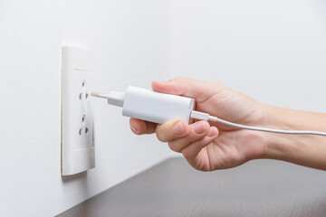 Female hand inserting a white electrical plug into outlet