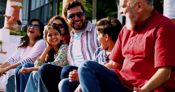 Indian family smiling on steps outdoors spending quality time together on green lawn, cheerful multi-generation portrait of grandparents, parents, and kids bonding, relaxing, enjoying leisure weekend