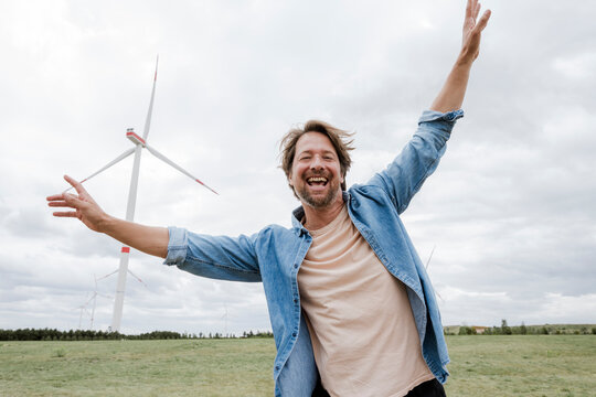 Smiling man dancing outdoors in front of wind turbine on a windy day