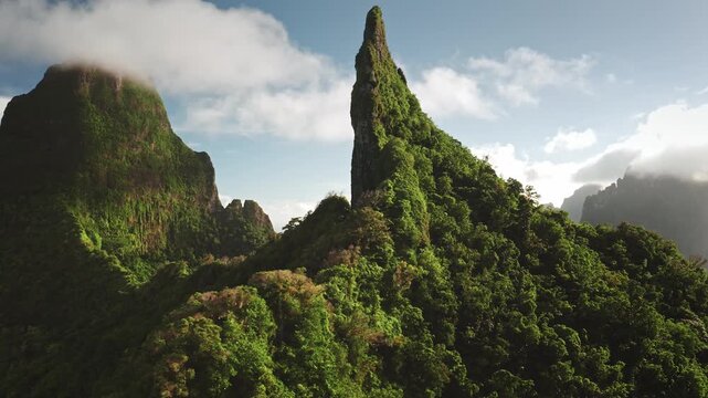Moorea island dramatic volcanic mountain peaks blanketed in vibrant green rainforest foliage under a partly cloudy blue sky, highlighting the rich natural beauty of French Polynesia. Aerial panorama