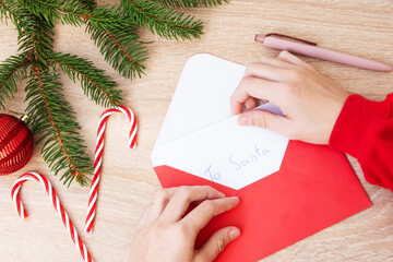 A child's hand is putting a Christmas letter with wishes for Santa Claus into a red envelope. New...