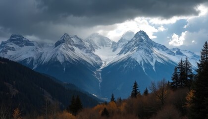 Snowy mountains under cloudy sky. Dark forest and yellow bushes. Scenic landscape photo of Alps mountains in winter. Nature view of mountain peaks and hills.