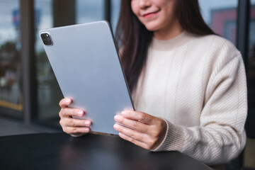Closeup image of a woman holding and using digital tablet in cafe