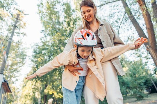 Mother supporting daughter rollerblading in park wearing helmet