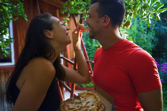 Couple feeding each other pizza outdoors in summer with joyful expressions