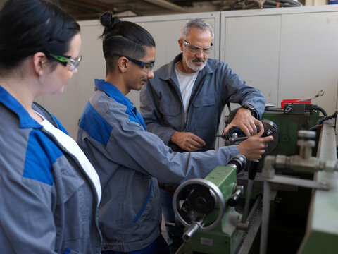 Trainees learning to use lathe machine with instructor at workshop