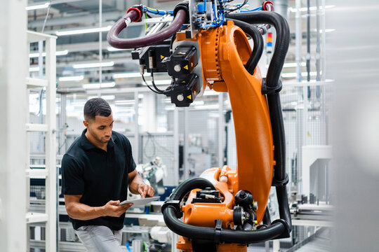 Businessman using digital tablet at industrial robot in a factory