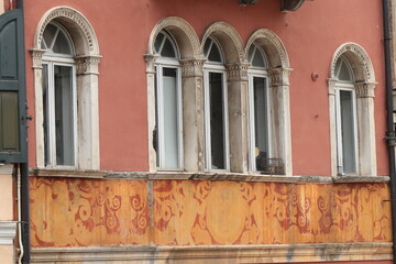 Pink Building Facade Detail with Arched Windows and Yellow and Red Painted Decoration in Udine, Italy