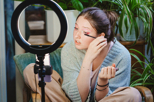 Vlogger applying mascara and recording video on smart phone on balcony