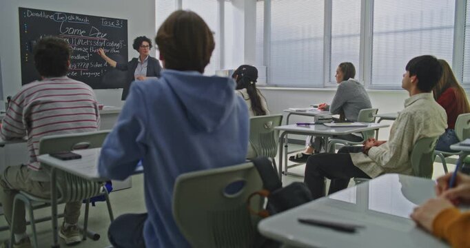 Confident Female Teacher Explains Coding Tasks to Students. Teenagers Listen Attentively, Take Notes, and Discuss Ideas. Modern STEM Education, Teamwork, Innovative Learning Environment. Dolly Shot.