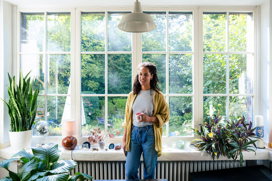 Smiling young woman standing in front of window at home