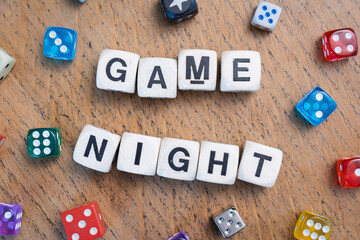 GAME NIGHT spelt using wooden word dice with vibrant dice around set over a pale wooden tabletop background - perfect for promoting game events or fun family gatherings.