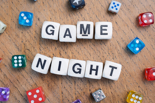 GAME NIGHT spelt using wooden word dice with vibrant dice around set over a pale wooden tabletop background - perfect for promoting game events or fun family gatherings.