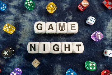 GAME NIGHT spelt using wooden word dice with vibrant dice set over a swirly blurred fabric background - perfect for promoting game events or fun family gatherings.