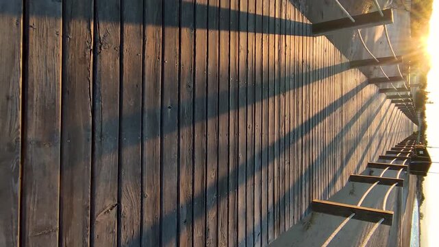 Strolling at sunset along a wooden boardwalk over the beach dunes. Wooden walkways installed to protect the dunes and their flora and fauna, on Riumar beach in Catalonia, Spain. Vertical.