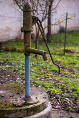 Old manual water pump in rural garden. Vintage hand pump with rust and moss showing traditional way of drawing water.