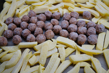 Frozen meatballs and french fries on a baking sheet, ready to cook
