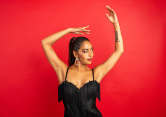 Young woman performing a passionate dance pose with arms raised in a black fringe dress