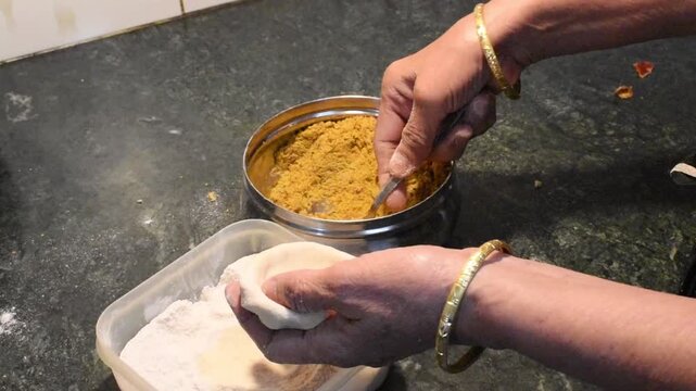 Lady&rsquo;s hand stuffing sattu mixture (roasted gram flour filling) into wheat dough balls for making Litti or Sattu Paratha in an Indian kitchen. traditional cooking process and kitchen activity