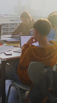 Young Pupils Deeply Concentrated Around Shared Table, Working on Group Project Using Mix Laptops, Tablets, Notebooks. Concept Digital Learning, Teamwork in Modern Learning Environment. Vertical Shot.