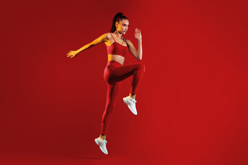 A fit woman is captured mid-jump in striking red activewear on a vivid red background, showcasing...