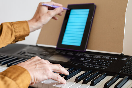 Closeup of young man learning to play keyboard at home using an interactive app. Man playing keyboard and using digital sheet music on electronic tablet - Powered by Adobe