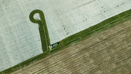 Aerial view of a tractor carving a vivid green path through fields of contrasting plowed land and snow, Đakovo, Osijek-Baranja County, Croatia.