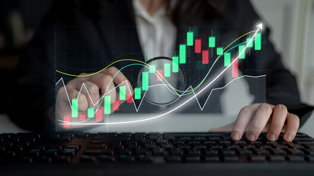 Business professional engages in stock market analysis with graphical data displayed on a computer, emphasizing growth and investment opportunities in a dynamic workspace setting. Impute