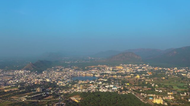 A peaceful cinematic landscape view of Pushkar city and lake surrounded by the Aravalli mountains at sunset. The soft evening colors and spiritual atmosphere showcase the essence of Rajasthan.