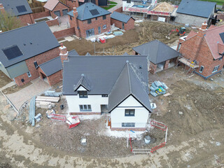 Drone view of a near completed large, detached family home on a British housing development site in rural Britain. Small houses can be seen in the background.