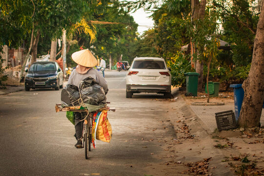 vietnamese street view with a woman on a bicycle carrying bags, cars parked along the road