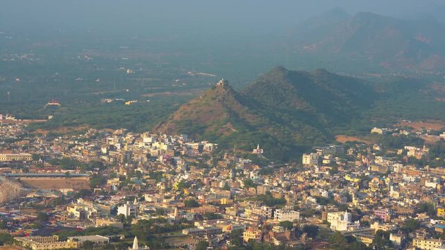 A stunning aerial shot showing the sacred town of Pushkar nestled amidst the Aravalli range. The calm lake, temples, and desert hills together create a serene and cinematic landscape.
