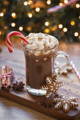 Cup of hot chocolate with marshmallow and candy cane in front of Christmas tree