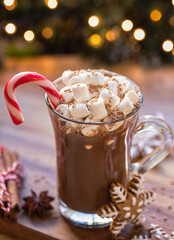 Cup of hot chocolate with marshmallow and candy cane in front of Christmas tree